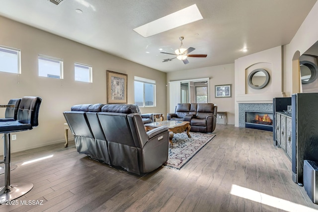 living area featuring a ceiling fan, a skylight, dark wood-style floors, and a tile fireplace