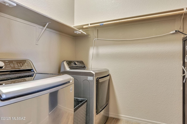washroom with washing machine and clothes dryer, laundry area, a textured wall, baseboards, and wood finished floors