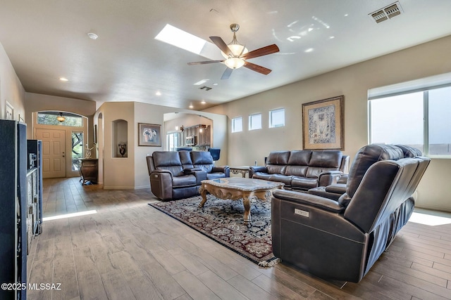 living room with arched walkways, a ceiling fan, baseboards, wood finished floors, and visible vents