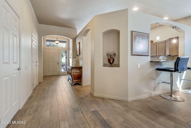 foyer featuring light wood-style floors, arched walkways, baseboards, and vaulted ceiling