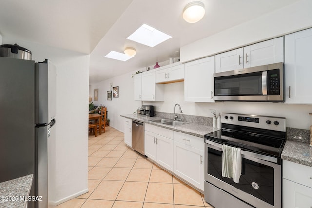 kitchen with a skylight, appliances with stainless steel finishes, a sink, white cabinets, and light tile patterned flooring