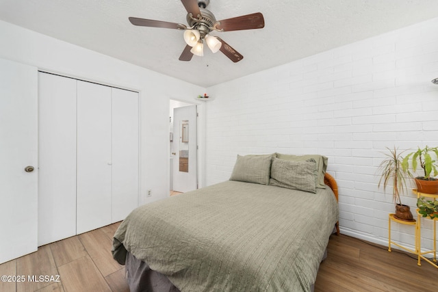 bedroom with a ceiling fan, a closet, brick wall, and wood finished floors