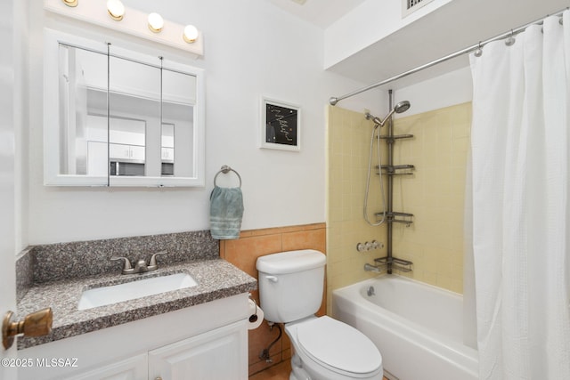 full bath featuring vanity, wainscoting, toilet, tile walls, and shower / bath combo