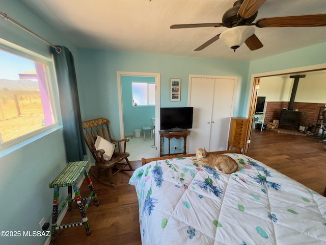 bedroom featuring connected bathroom, a wood stove, ceiling fan, and wood finished floors