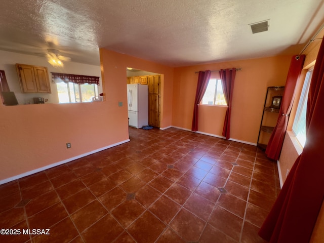 unfurnished room featuring a textured ceiling, visible vents, dark tile patterned floors, and baseboards