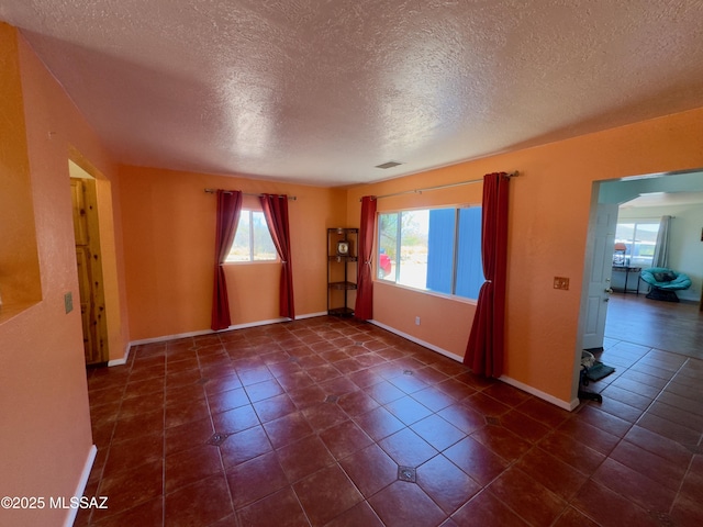 spare room featuring a textured ceiling, dark tile patterned flooring, visible vents, and baseboards