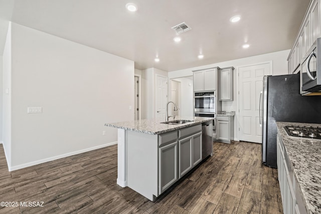 kitchen with stainless steel appliances, gray cabinets, an island with sink, and a sink