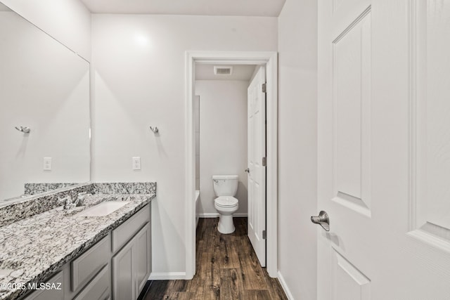 full bath featuring vanity, wood finished floors, toilet, baseboards, and a bath