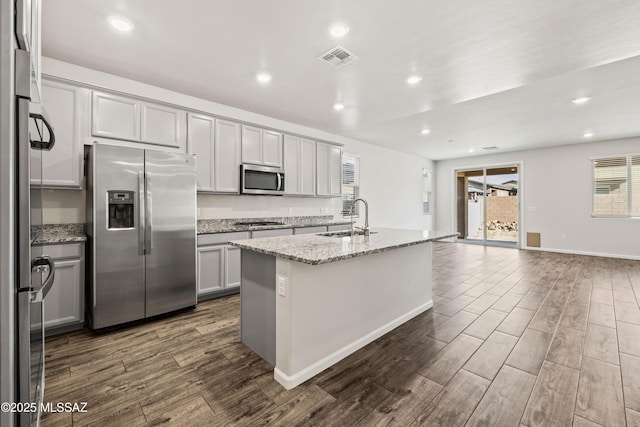 kitchen with gray cabinets, a kitchen island with sink, appliances with stainless steel finishes, a sink, and dark wood-type flooring