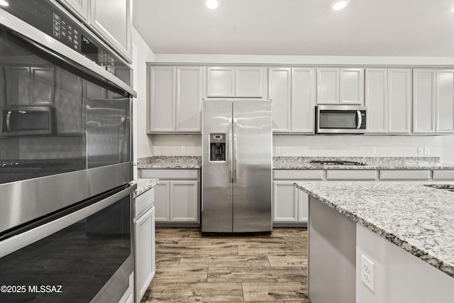 kitchen featuring light wood-type flooring, recessed lighting, appliances with stainless steel finishes, and light stone counters
