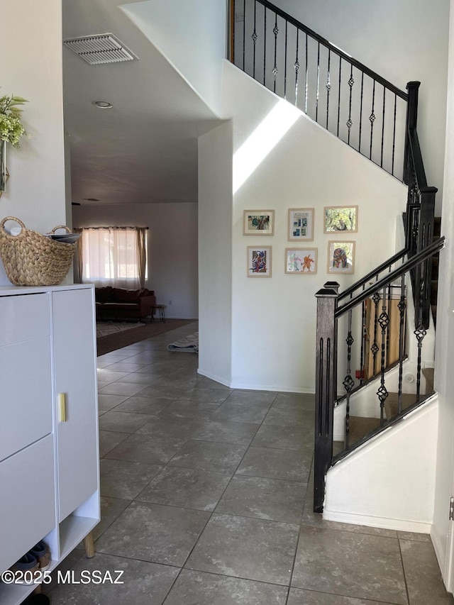staircase featuring baseboards, a high ceiling, and visible vents
