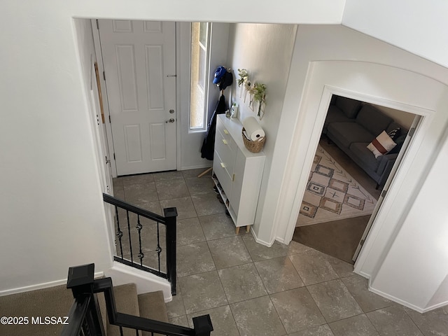 hallway featuring dark tile patterned floors, baseboards, and stairs