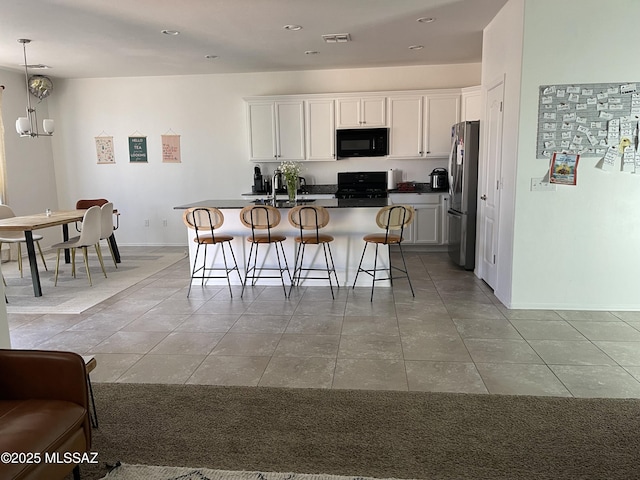 kitchen featuring a kitchen breakfast bar, black microwave, a center island, gas stove, and freestanding refrigerator