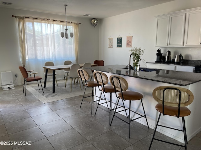 kitchen with white cabinets, a sink, dark stone countertops, a kitchen bar, and visible vents