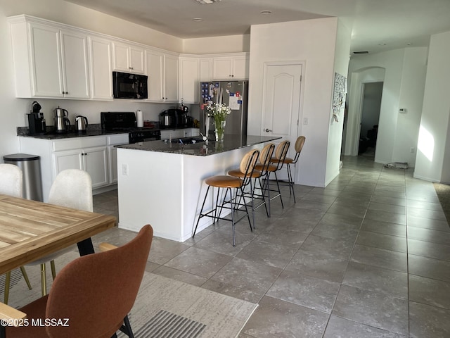 kitchen featuring arched walkways, white cabinetry, a kitchen bar, a kitchen island, and black appliances