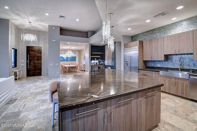 kitchen with stone tile floors, a sink, visible vents, stainless steel appliances, and a notable chandelier