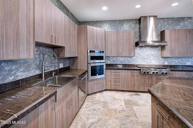 kitchen featuring decorative backsplash, appliances with stainless steel finishes, wall chimney range hood, and a sink