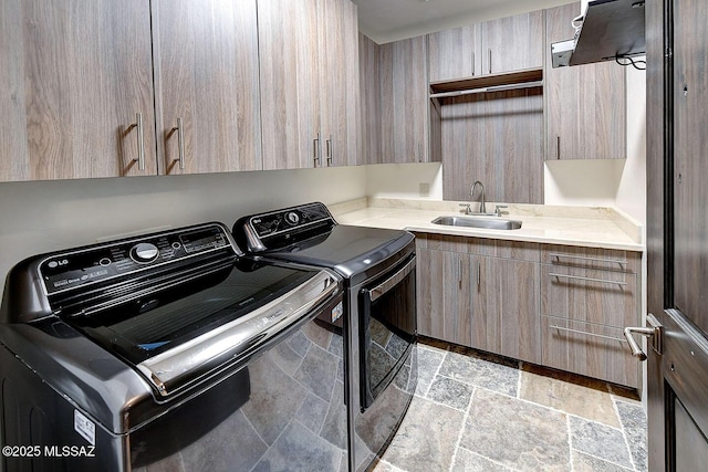 clothes washing area with washer and dryer, stone tile flooring, cabinet space, and a sink