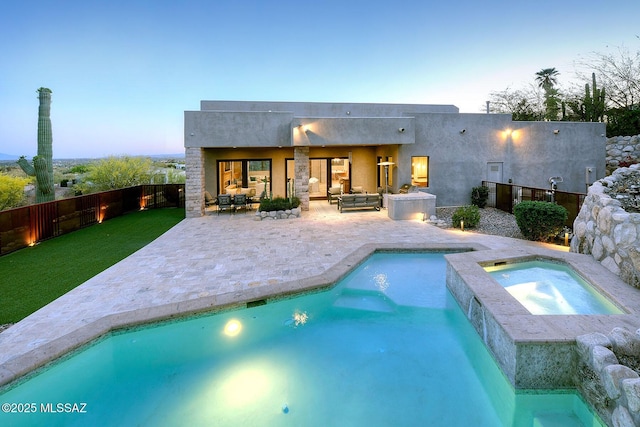 back of property at dusk with outdoor lounge area, a fenced in pool, an in ground hot tub, and a patio area
