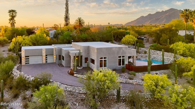 pueblo revival-style home featuring an attached garage, a mountain view, driveway, and stucco siding