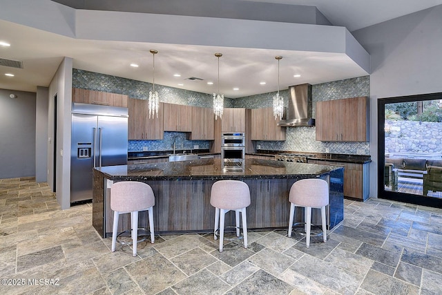 kitchen with stone tile floors, stainless steel appliances, decorative backsplash, and wall chimney exhaust hood