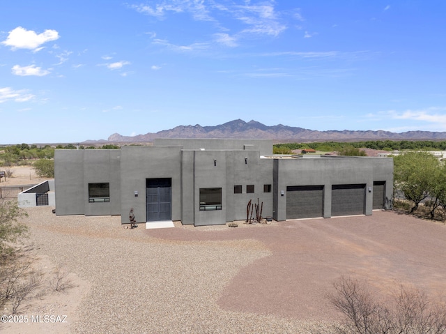 pueblo revival-style home featuring dirt driveway, a garage, a mountain view, and stucco siding
