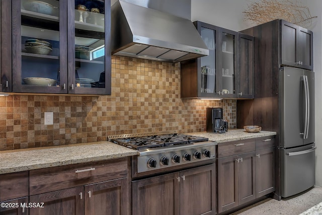 kitchen featuring appliances with stainless steel finishes, light stone counters, dark brown cabinetry, and wall chimney exhaust hood