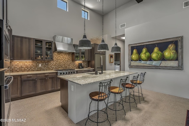 kitchen with wall chimney range hood, visible vents, a sink, and a towering ceiling