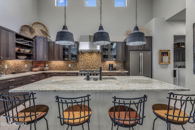 kitchen with wall chimney range hood, plenty of natural light, dark brown cabinetry, a sink, and freestanding refrigerator