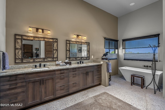bathroom with speckled floor, double vanity, a freestanding tub, and a sink