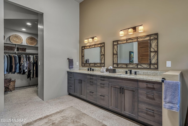 bathroom with double vanity, a walk in closet, visible vents, speckled floor, and a sink