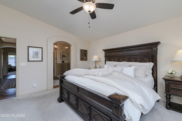 bedroom featuring arched walkways, ceiling fan, light carpet, and ensuite bath