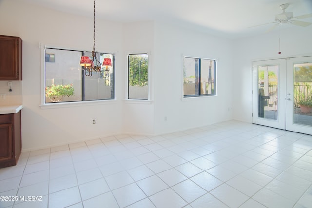 unfurnished dining area with french doors, baseboards, ceiling fan with notable chandelier, and a wealth of natural light