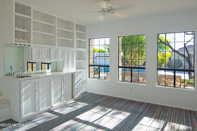 unfurnished dining area with a ceiling fan, baseboards, a sink, and dark colored carpet