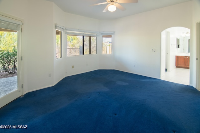 carpeted spare room with a ceiling fan, arched walkways, and baseboards