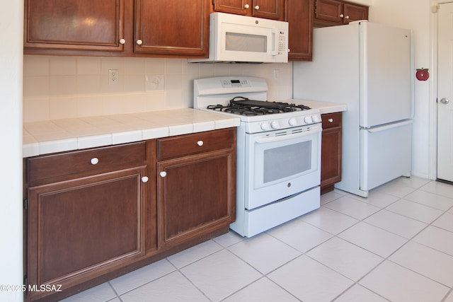 kitchen featuring white appliances, tile countertops, light tile patterned flooring, and tasteful backsplash