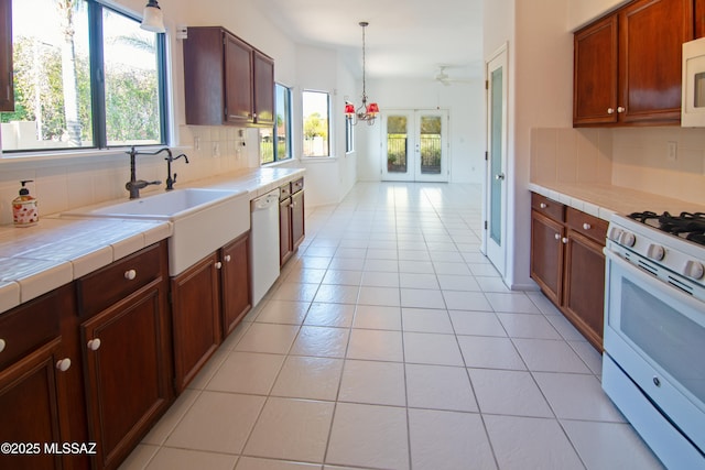 kitchen featuring white appliances, tile counters, a healthy amount of sunlight, and backsplash