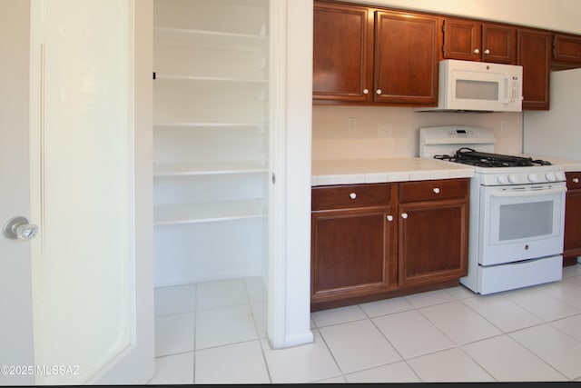 kitchen featuring white appliances, tile counters, light tile patterned floors, and tasteful backsplash