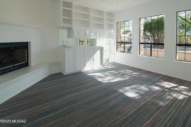 unfurnished living room with dark carpet, baseboards, a tiled fireplace, a sink, and wet bar