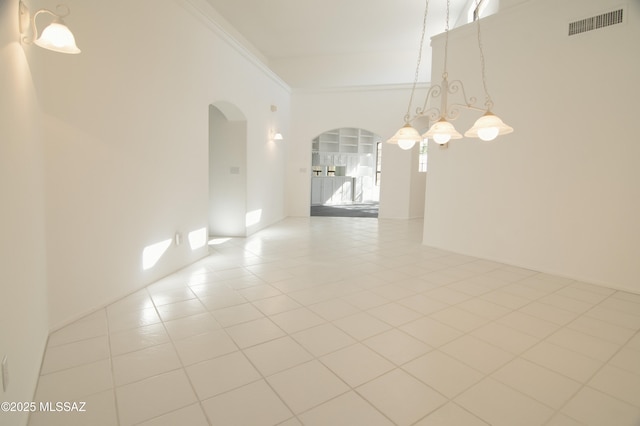 empty room featuring visible vents, crown molding, arched walkways, tile patterned floors, and a notable chandelier