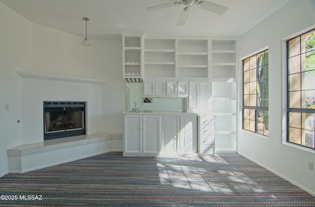 unfurnished living room featuring carpet floors, a tiled fireplace, indoor wet bar, a ceiling fan, and baseboards
