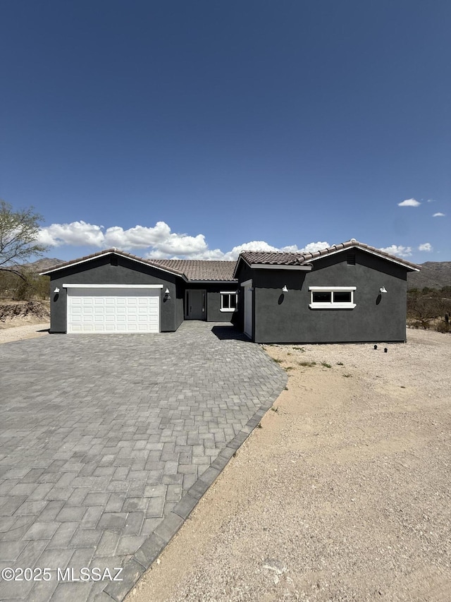 view of front facade with a tile roof, decorative driveway, an attached garage, and stucco siding