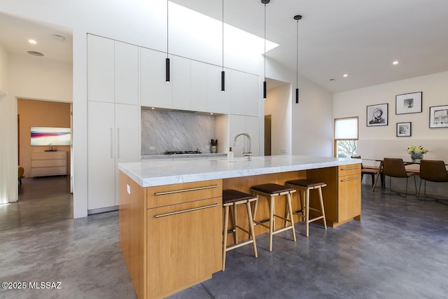 kitchen featuring modern cabinets, white cabinets, decorative backsplash, a large island with sink, and finished concrete flooring