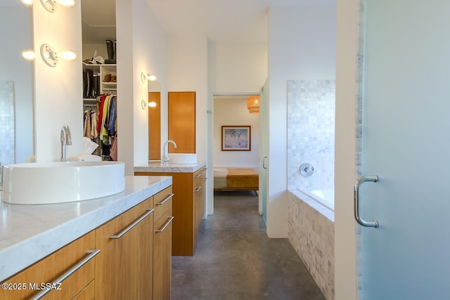 bathroom with connected bathroom, a sink, a relaxing tiled tub, two vanities, and concrete flooring