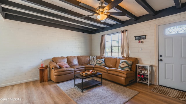 living room with a ceiling fan, brick wall, wood finished floors, baseboards, and beamed ceiling