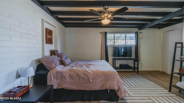 bedroom with a ceiling fan, wood finished floors, brick wall, and beam ceiling