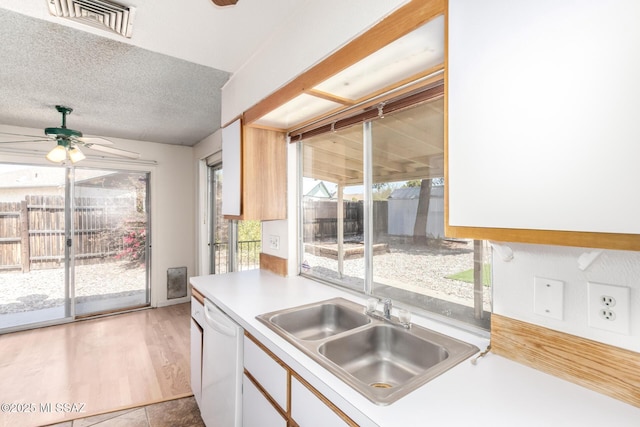 kitchen featuring a ceiling fan, visible vents, white dishwasher, a sink, and white cabinetry