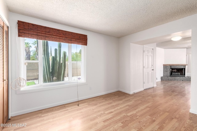 unfurnished room featuring baseboards, a fireplace with raised hearth, a textured ceiling, and wood finished floors