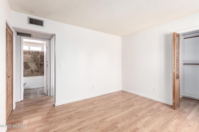 unfurnished bedroom with light wood-style floors, a closet, a textured ceiling, and visible vents