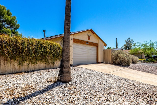 view of home's exterior featuring an attached garage, stucco siding, fence, and concrete driveway